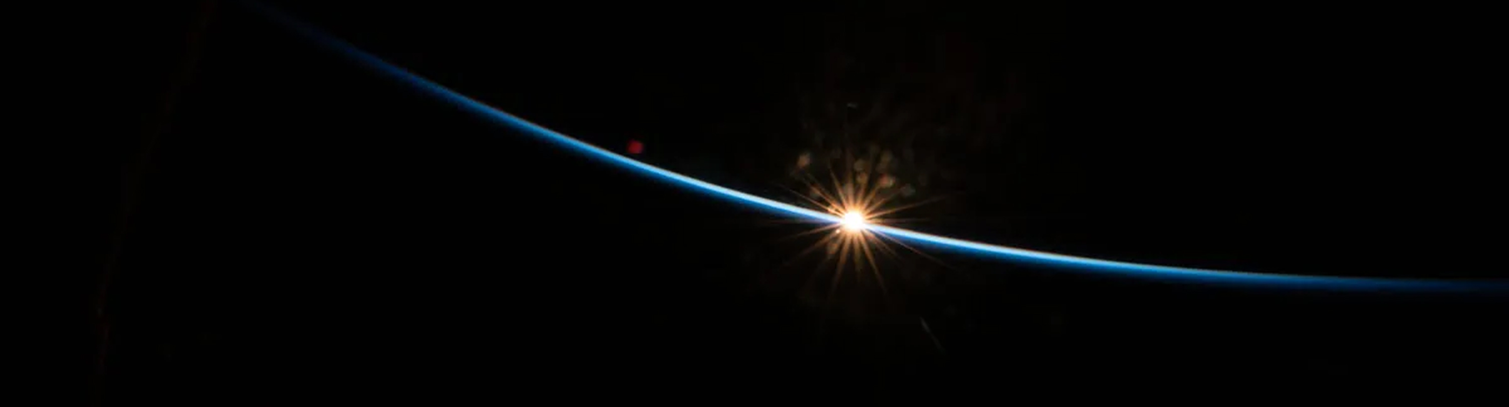 sun peeking over the horizon of earth in space